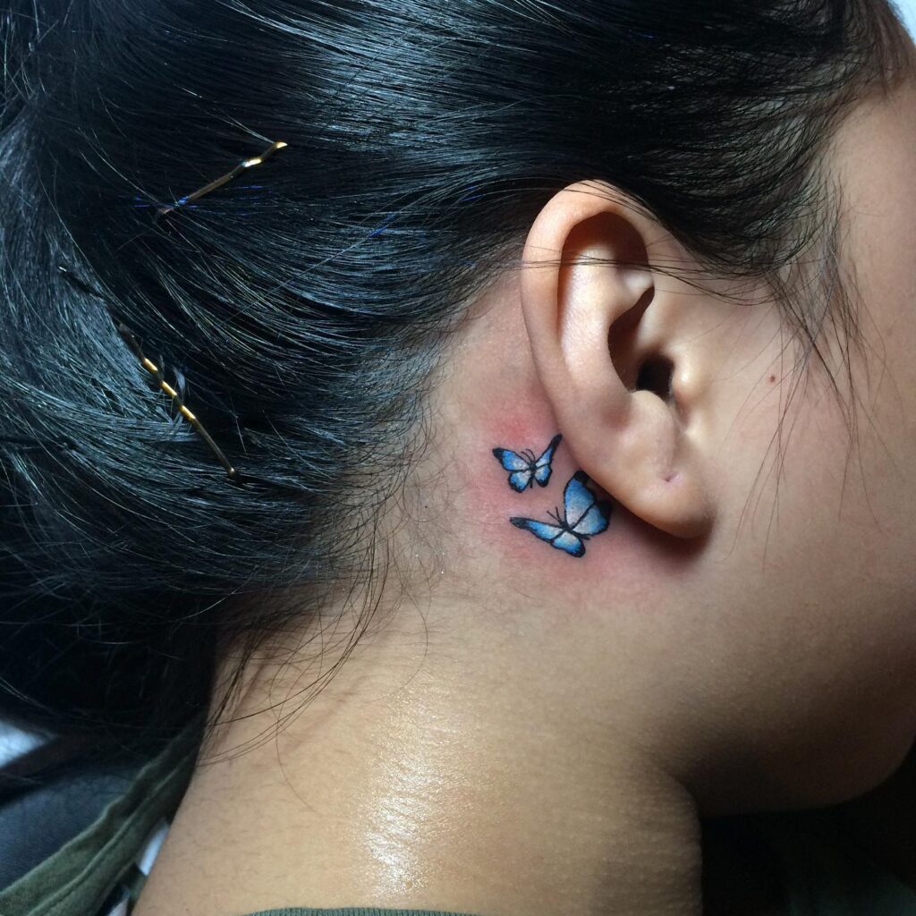 2 light blue butterflies flying together tattoo behind the ear girl serene elegance