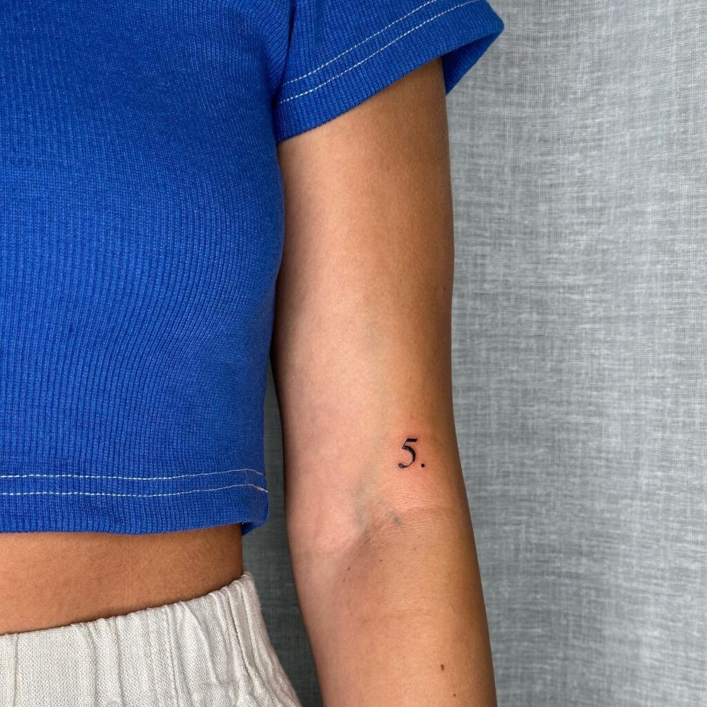 '5.' number tattoo above the inner elbow, thin, bold, and striking: bold numerics