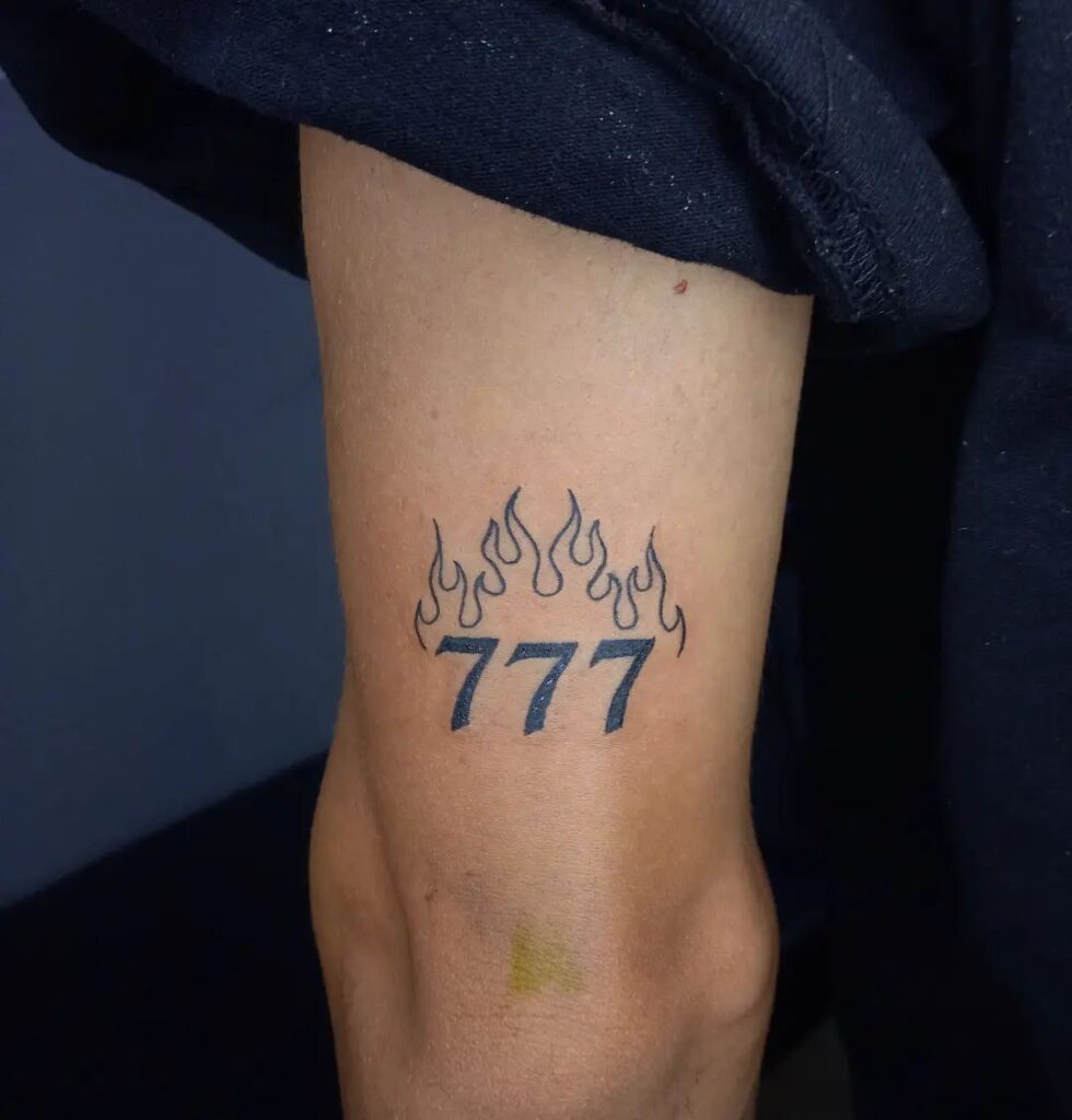 777 Tattoo with Fire Flame Accent on the Back of the Elbow: Flame Embrace