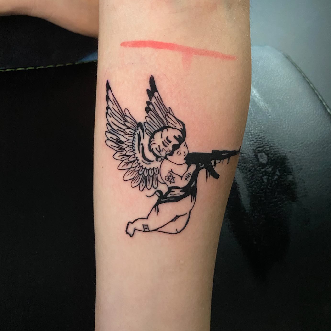 A Small Angel Tattoo Holding an Ak 47