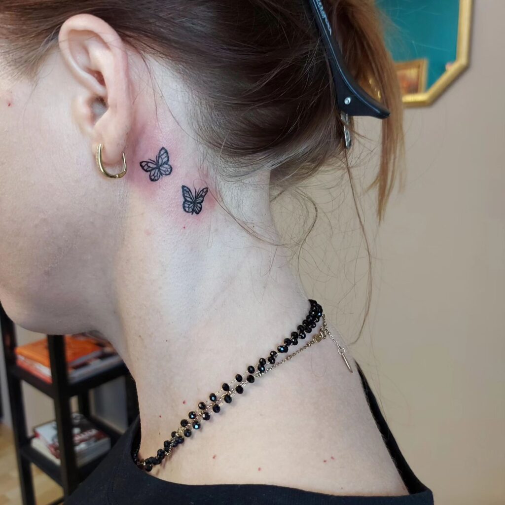 A pair of subtle elegance two black butterfly tattoos behind the ear