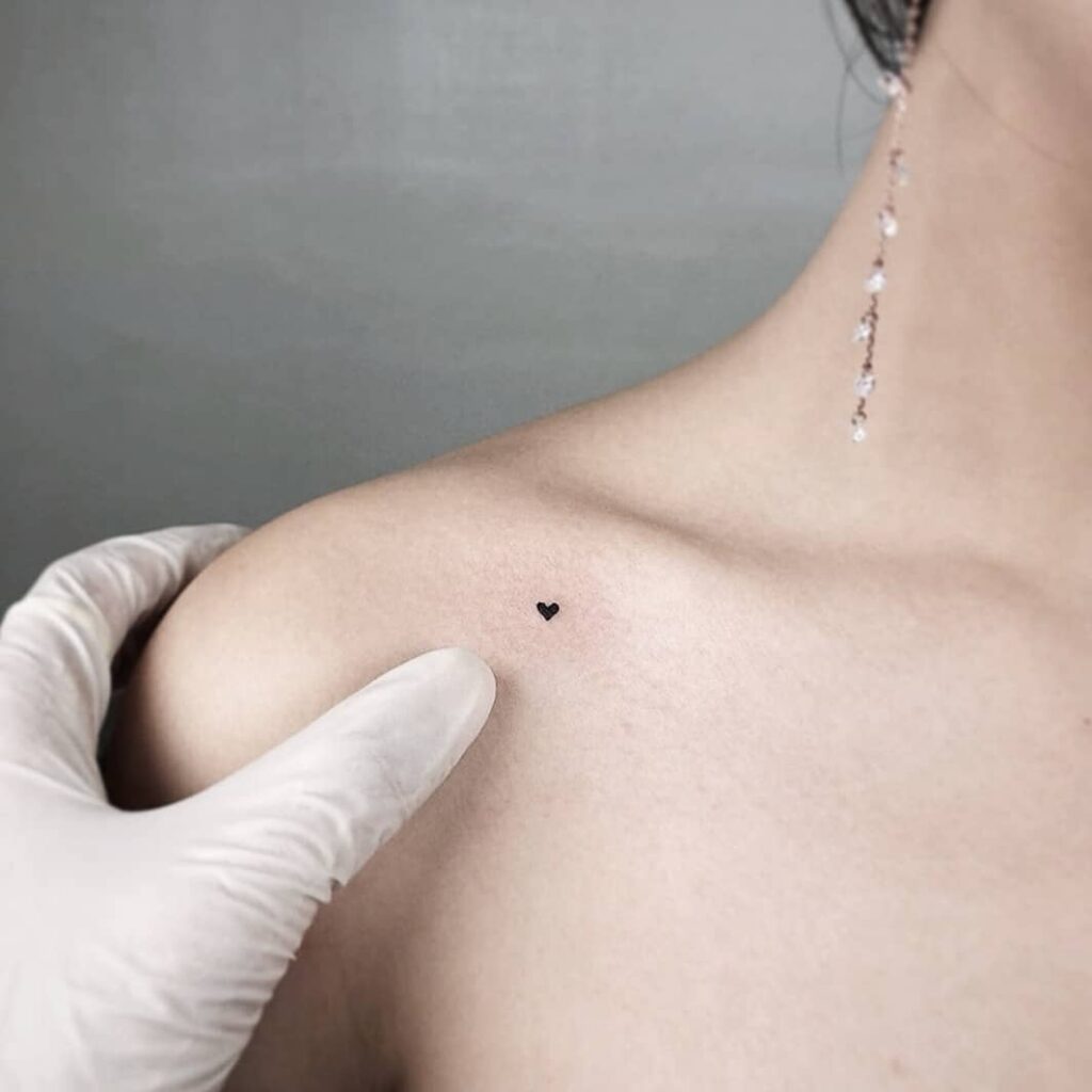 A tiny black love heart tattoo on the clavicle bone for a girl