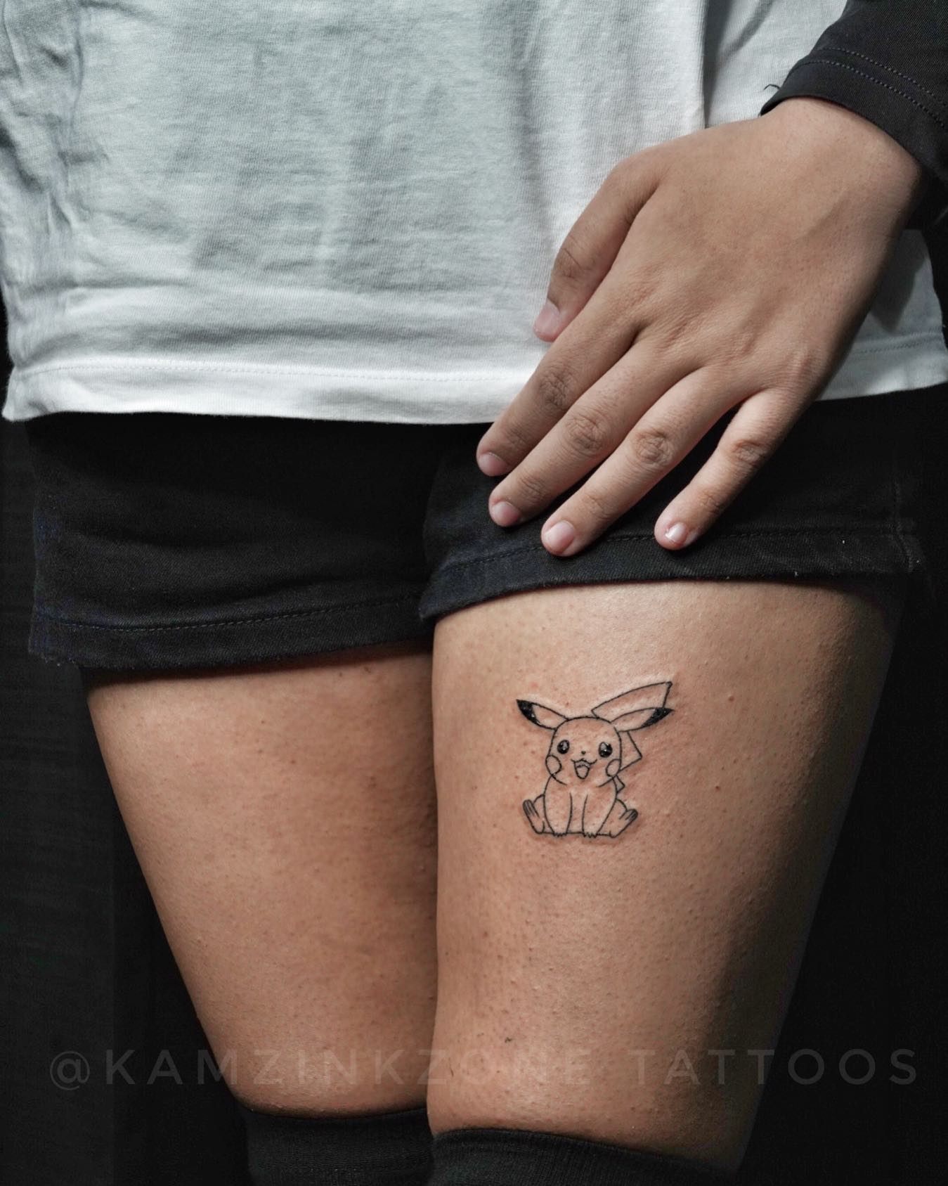 Adorable small Pikachu tattoo on the upper thigh, designed with fine-line details, representing energy, adventure, and the playful spirit of Pokémon lovers