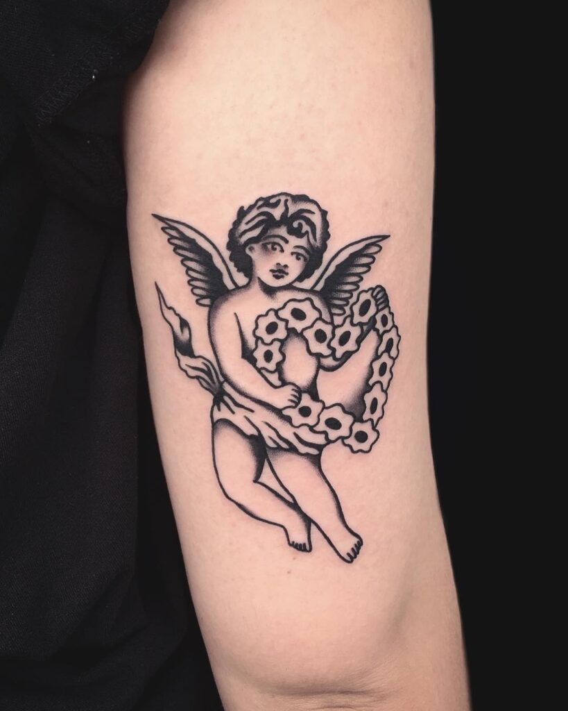 Angel holding heart-shaped tattoo on the outer arm above the elbow
