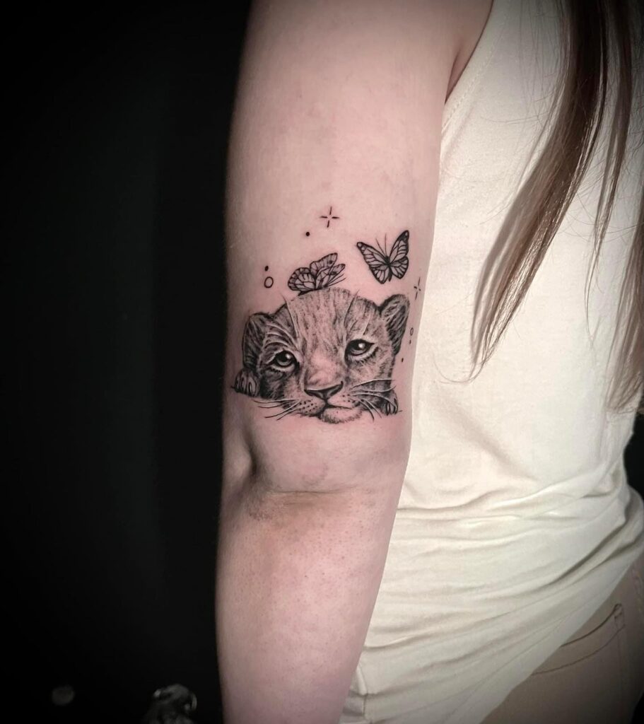 Baby cub tattoo on the back of the arm above the elbow with playful butterflies: cub charm