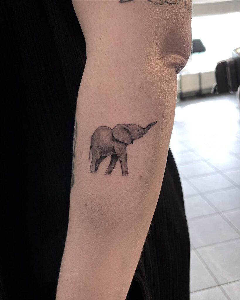Baby elephant side view tattoo lifting trunk on forearm: trunk lift charm