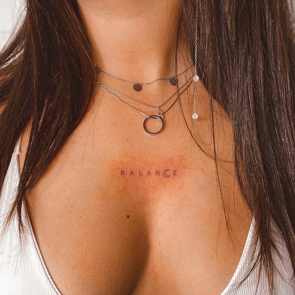 'Balance' word tattoo on the collarbone with a crescent moon replacing the letter 'c' celestial harmony
