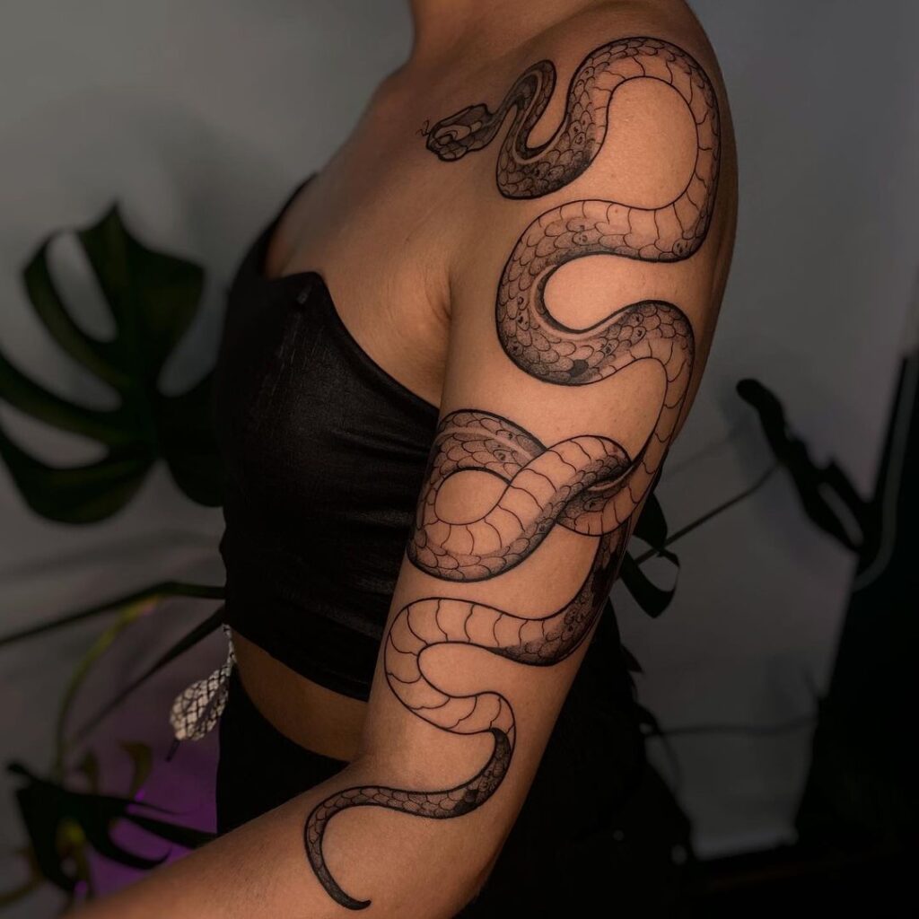 Black and gray tattoo of cobra along shoulder and arm fierce and feminine
