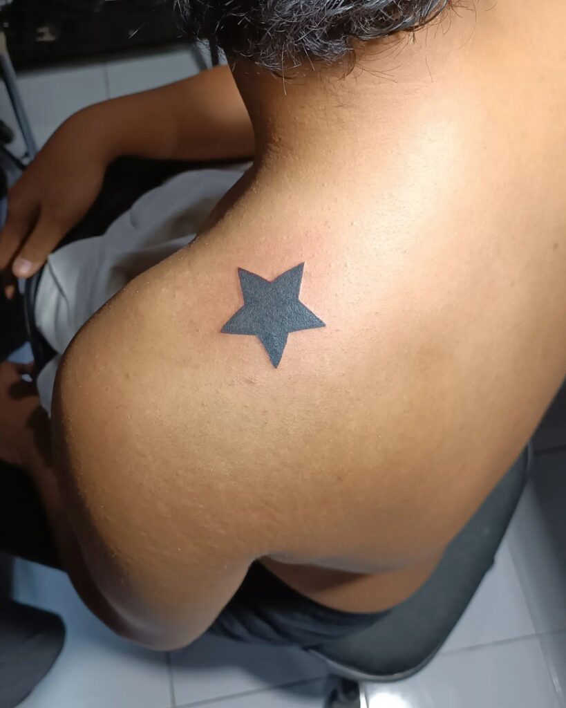 Black color filled single star tattoo on shoulder for women