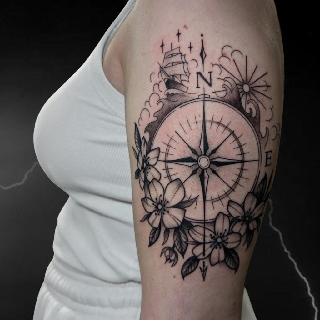 Black Work Compass Tattoo on the Upper Arm with Flowers, Ship, and Sea Details: Navigating Life