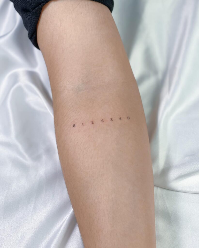 Blessed tattoo below the elbow, featuring letter spacing and thin font for a graceful effect: blessed serenity