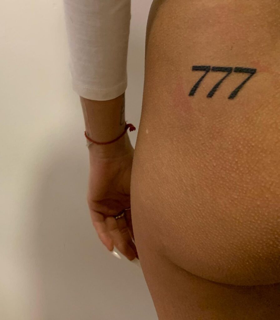 Bold 777 number tattoo on the buttock, creating a playful and unique placement cheeky seven trio 