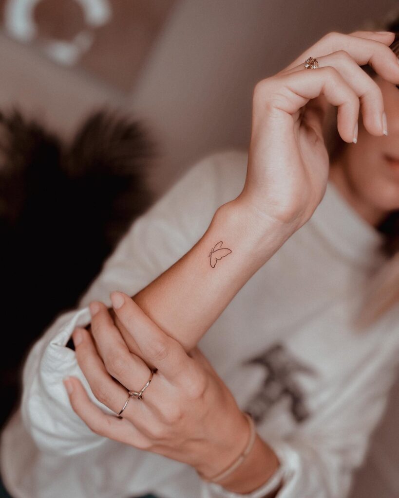 Butterfly side view wrist tattoo: mini outline butterfly in flight