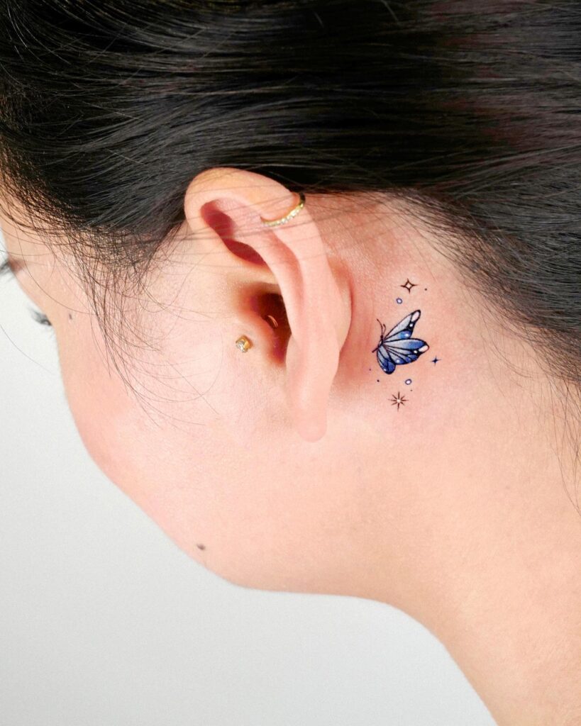 Celestial fusion stars harmonizing with a small blue butterfly tattoo behind the ear