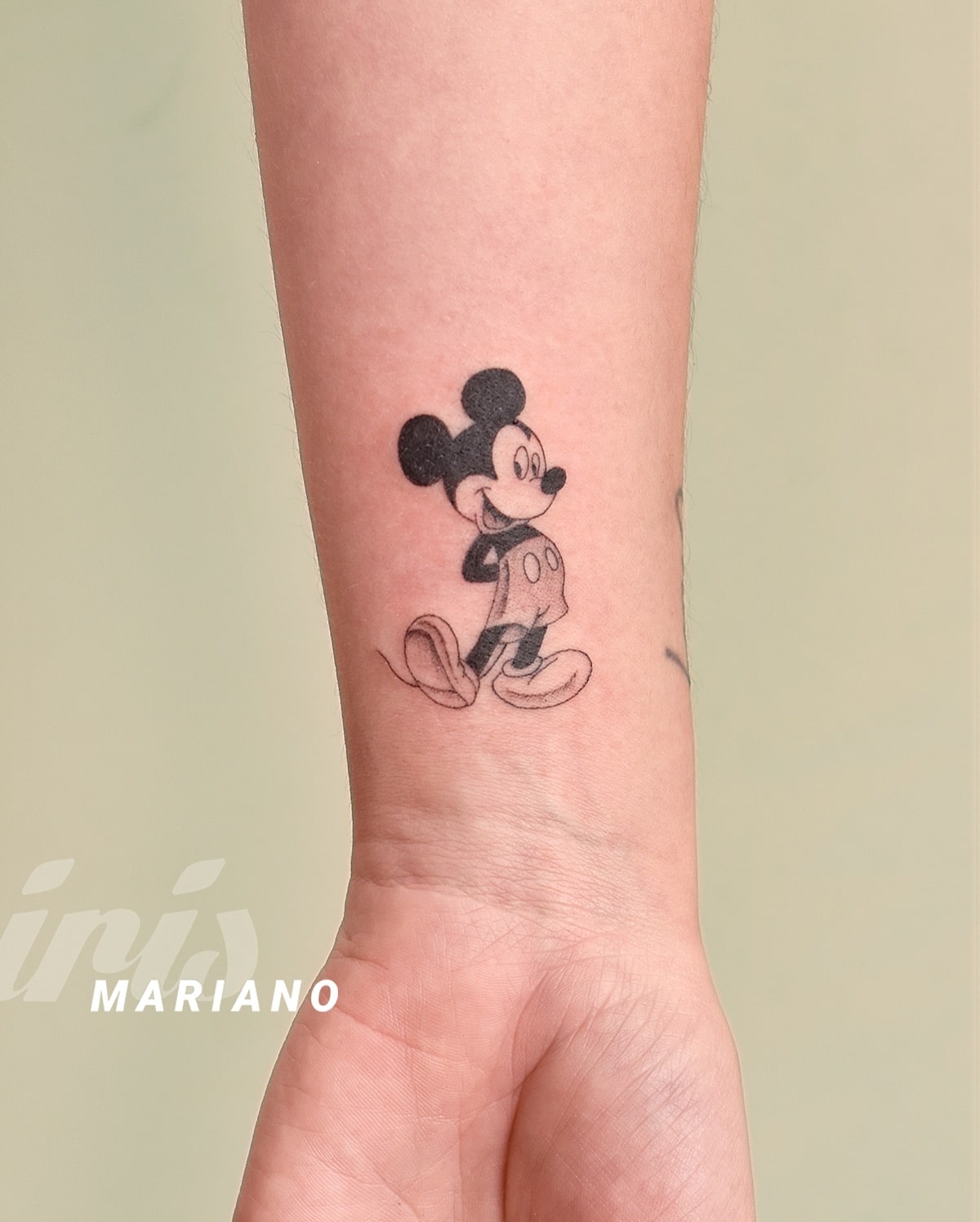Classic black-and-gray Mickey Mouse tattoo on the wrist, featuring vintage shading and cheerful expression, symbolizing joy, nostalgia, and childhood magic