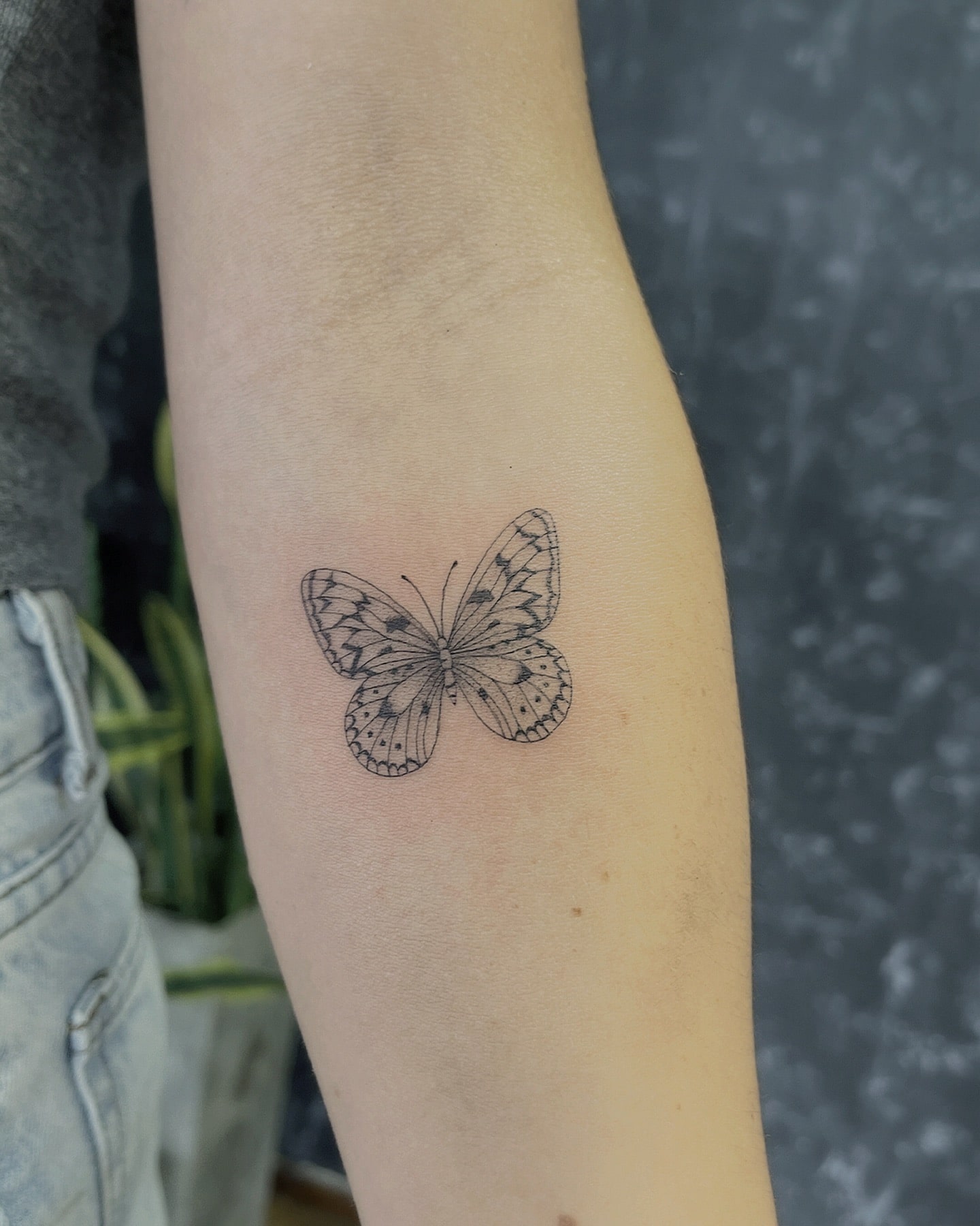 Classic black ink butterfly forearm tattoo with fine line details