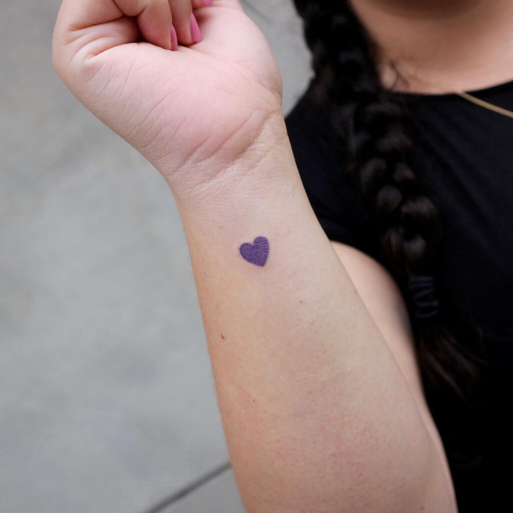 Classic heart tattoo on the side wrist, filled with a lovely purple hue for a feminine and vibrant look: purple passion