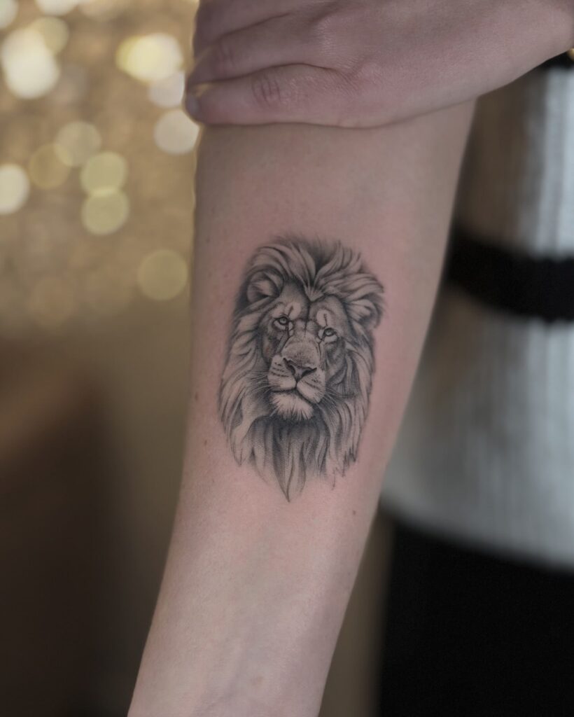 Classic lion face tattoo on the forearm detailed in grey shaded art for a royalty feel