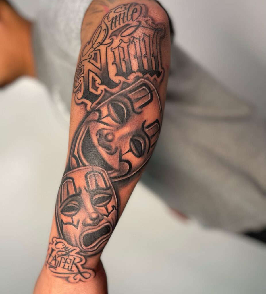 Classical masks with a message laugh now cry later outer forearm ink 