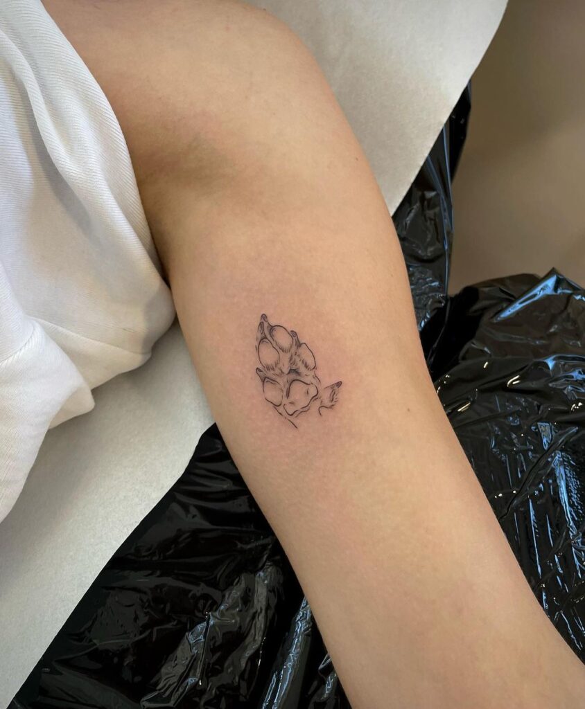 Clean and delicate fineline dog paw print tattoo on the female biceps