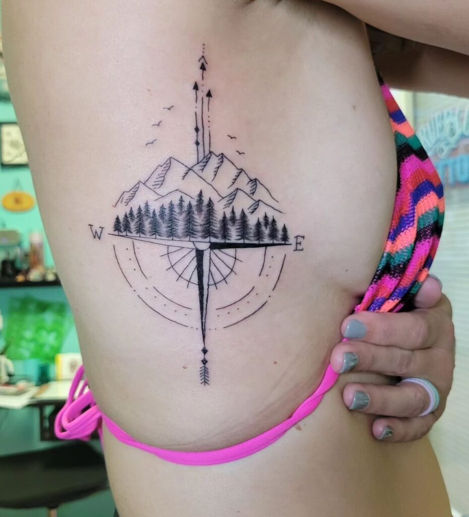 Compass Tattoo Above Mountains and Trees in Black and Grey on the Rib: Mountainous Direction