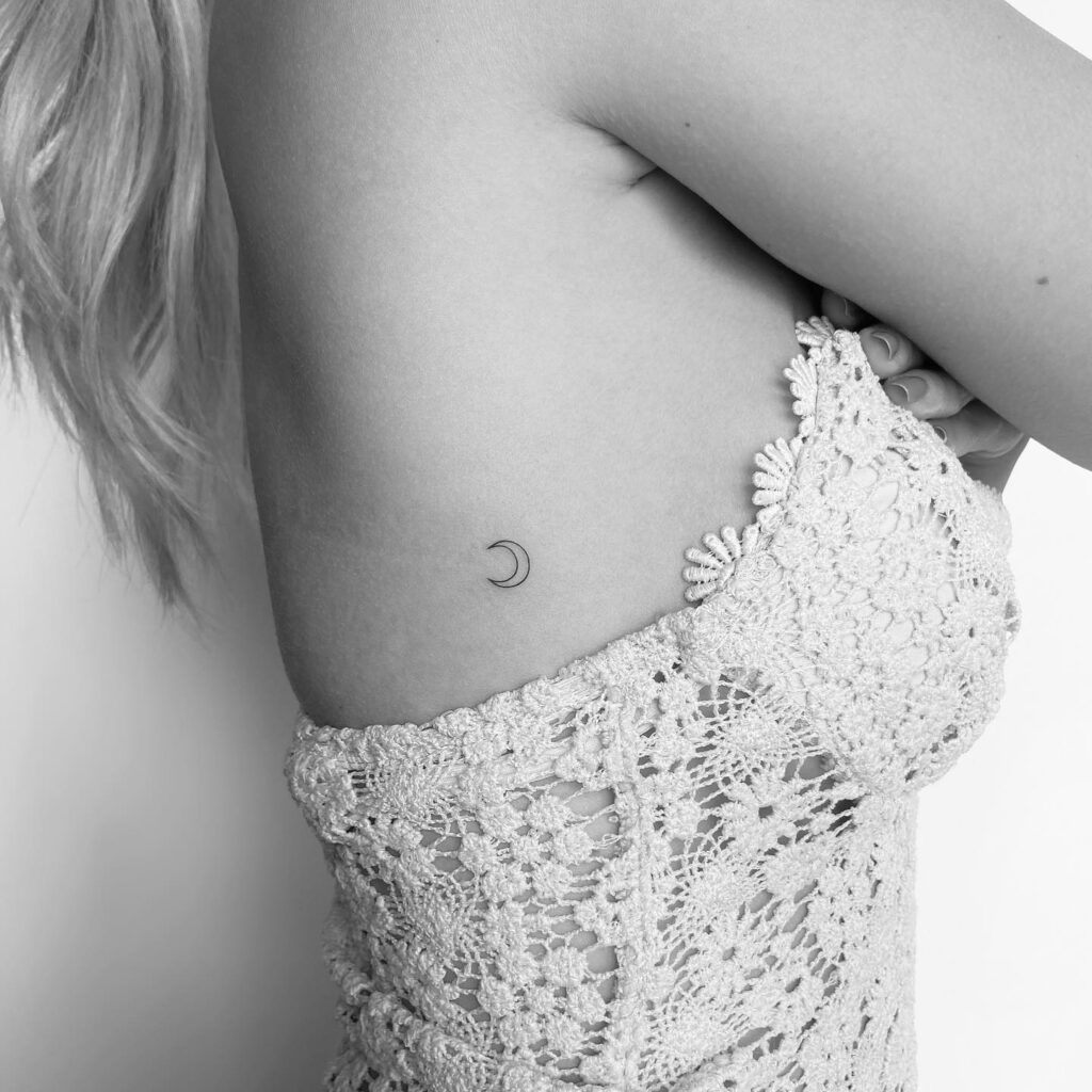 Crescent moon outline tattoo on the side rib, petite and subtle: lunar whispers