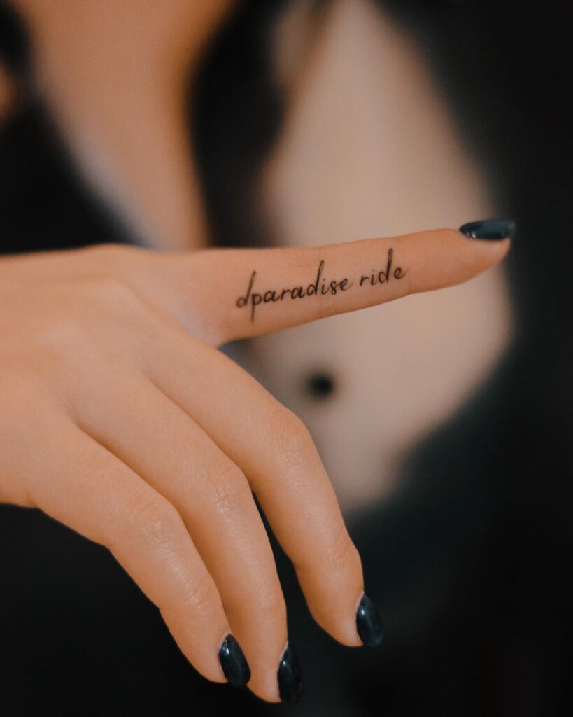Cute 'Dparadise Ride' Lettering Tattoo on the Side of the Forefinger for a Chic and Edgy Vibe: Paradise Ride