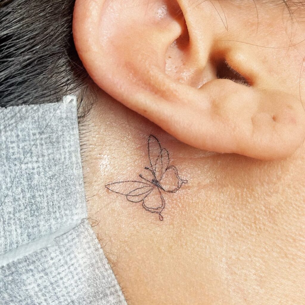 Cute and simple outline butterfly tattoo gracefully accenting the area behind the ear for women