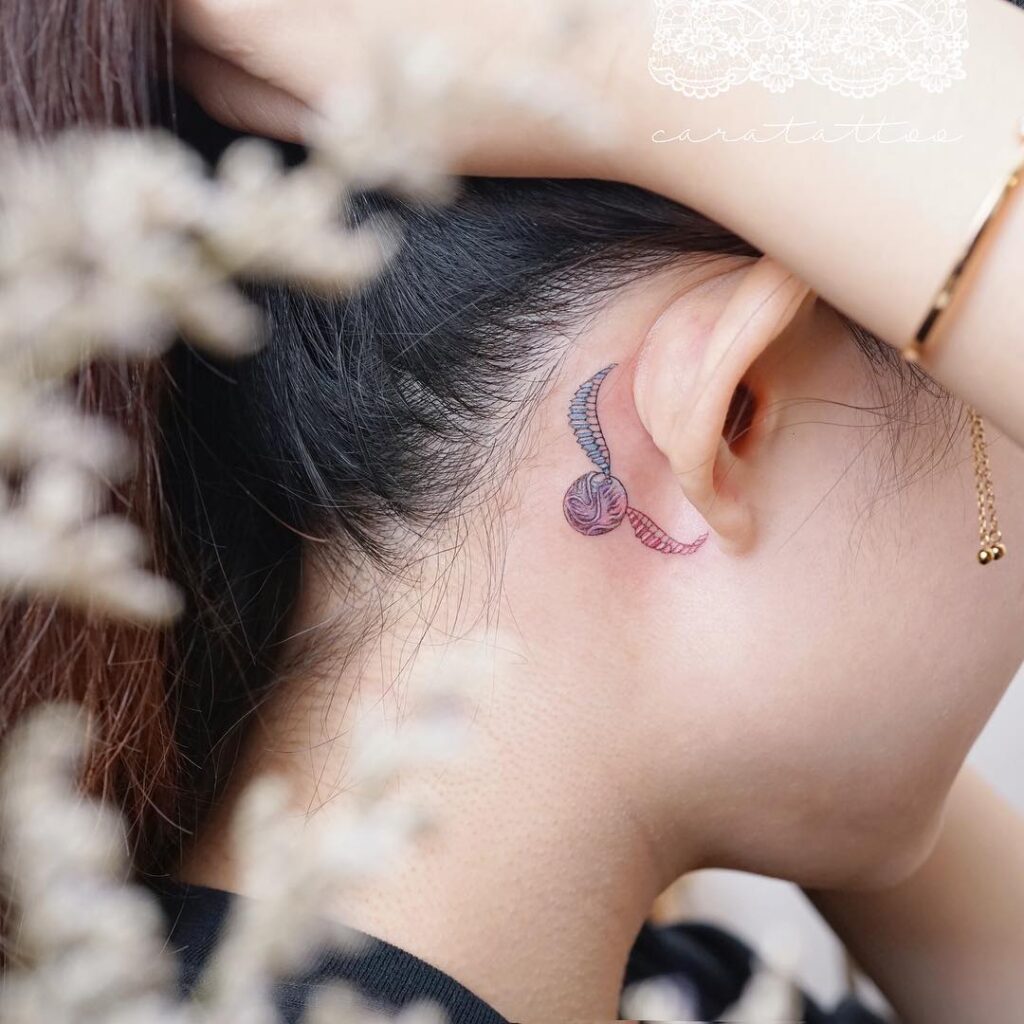 Cute behind the ear golden snitch tattoo for ladies whimsical beauty
