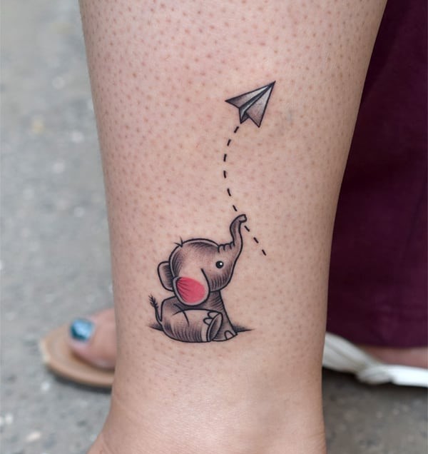 Cute elephant tattoo above the ankle with a paper plane, expressing love for travel wanderlust pachyderm