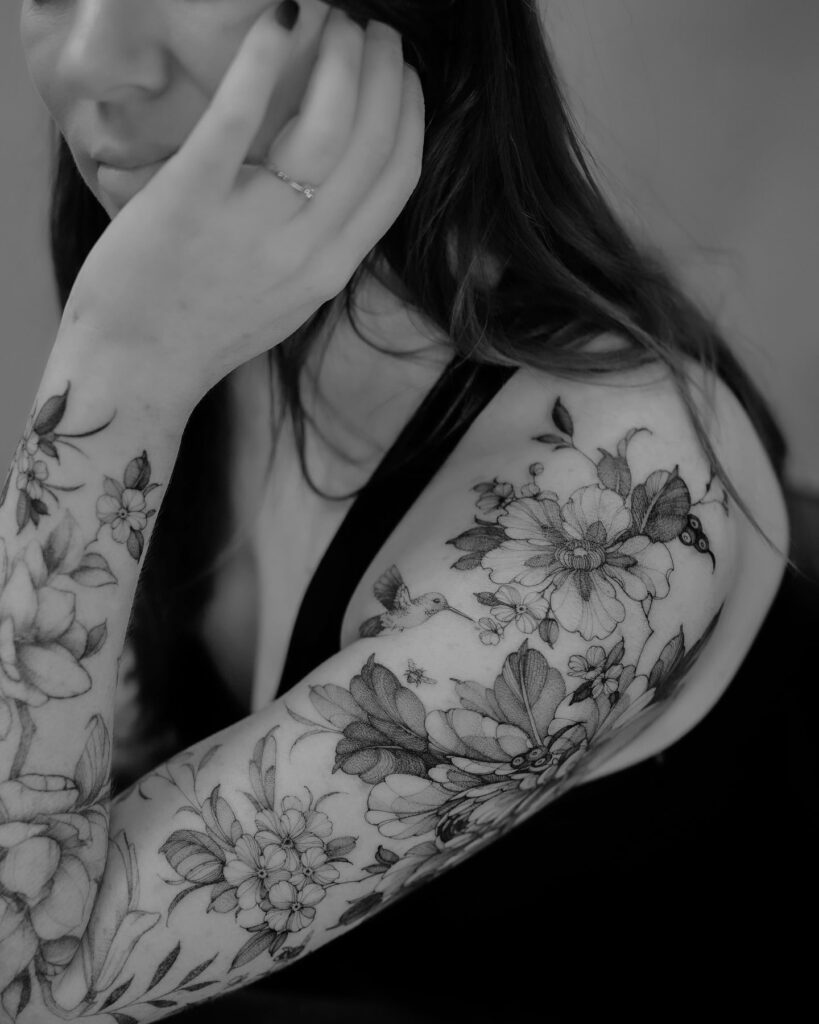Delicate botanical tattoo sleeve with a hummingbird and soft shading for females