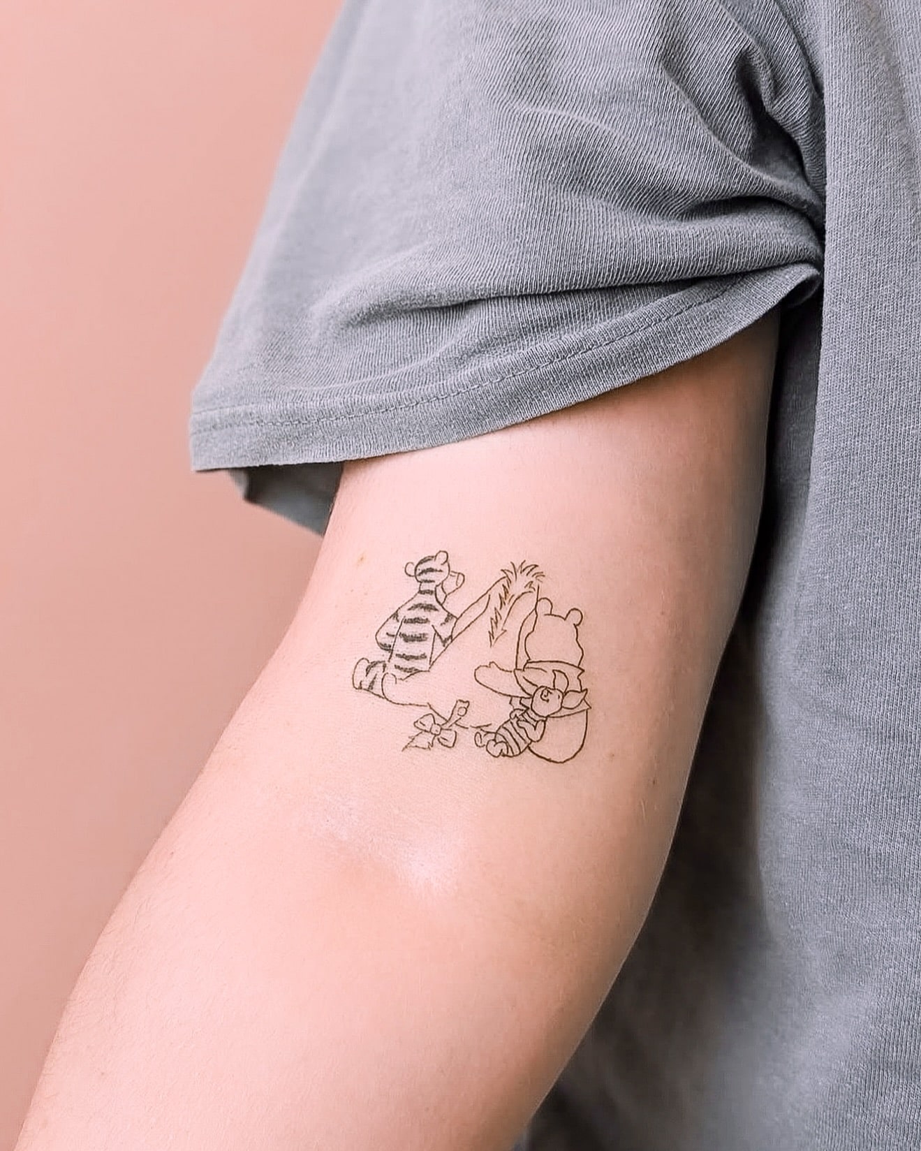 Delicate fine-line Winnie the Pooh and Tigger tattoo placed on the inner bicep, symbolizing nostalgia, childhood memories, and the value of true friendship