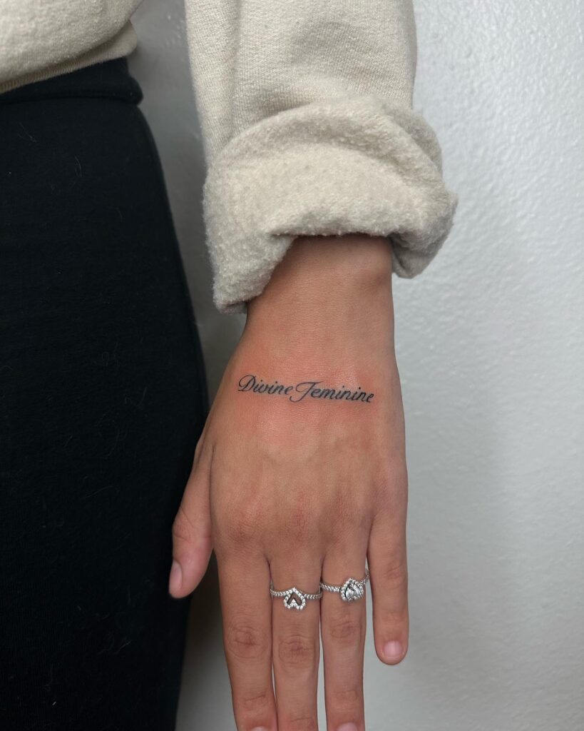 Divine feminine text cursive lettering tattoo on the hand empowerment and beauty