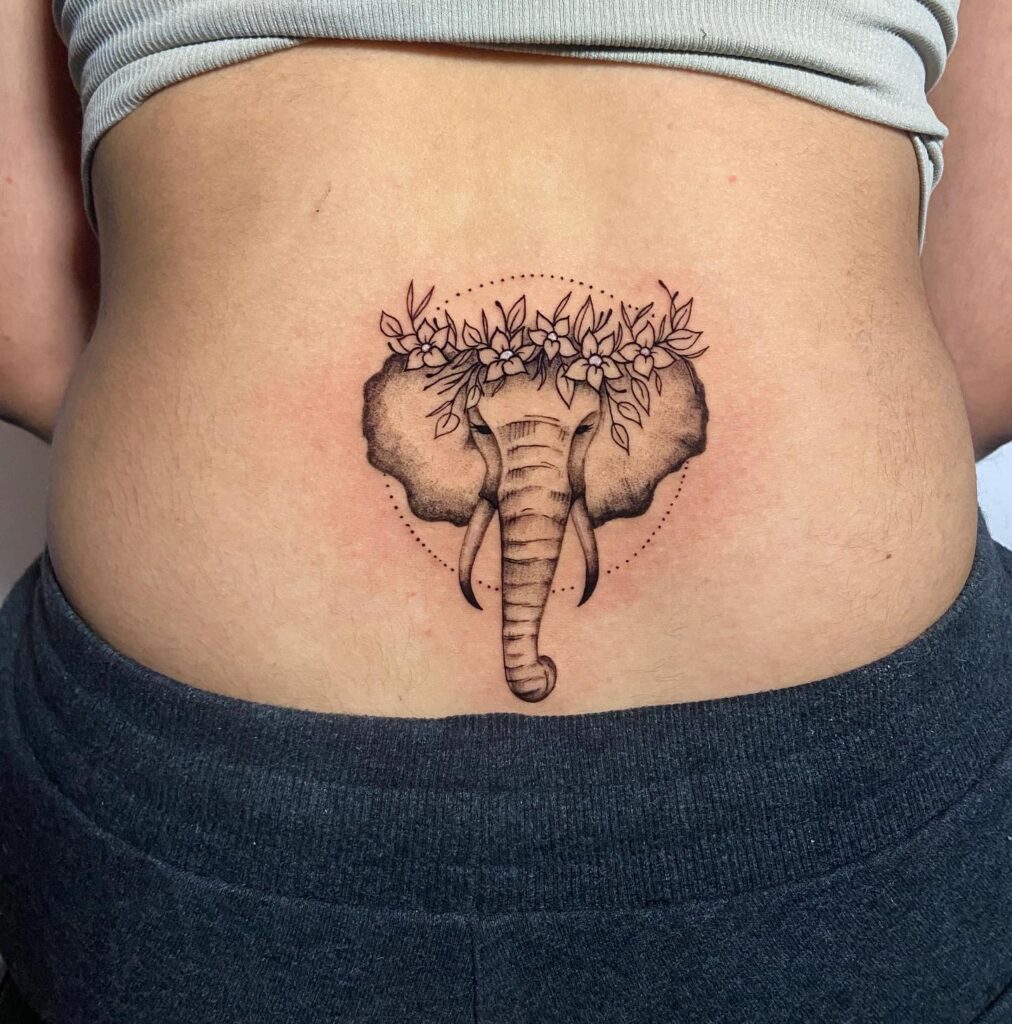 Elephant ears, tusk, and trunk lower back tattoo with surrounding flowers, a delicate composition floral majesty
