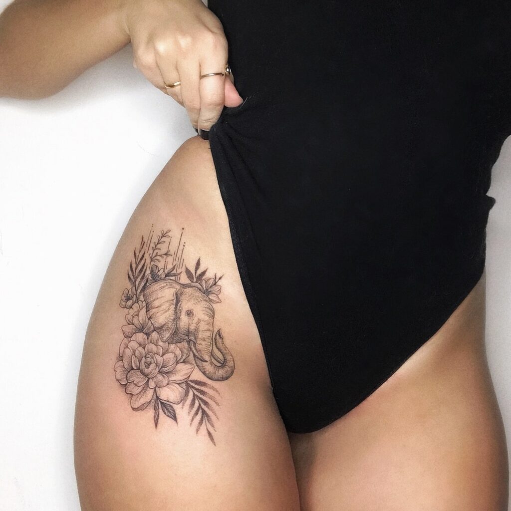 Elephant with flower hip and thigh tattoo in black and grey, the head surrounded by blooms botanical serenity