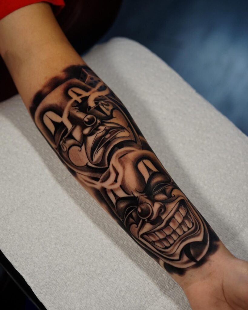 Embracing smiles and tears smile now cry later mask tattoo on inner forearm 