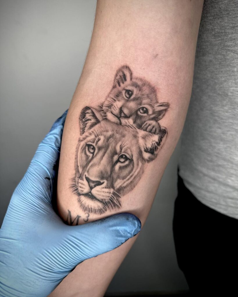 Family tattoo with female lion and cub on the forearm, showcasing the cute cub above the majestic lioness head family bonds