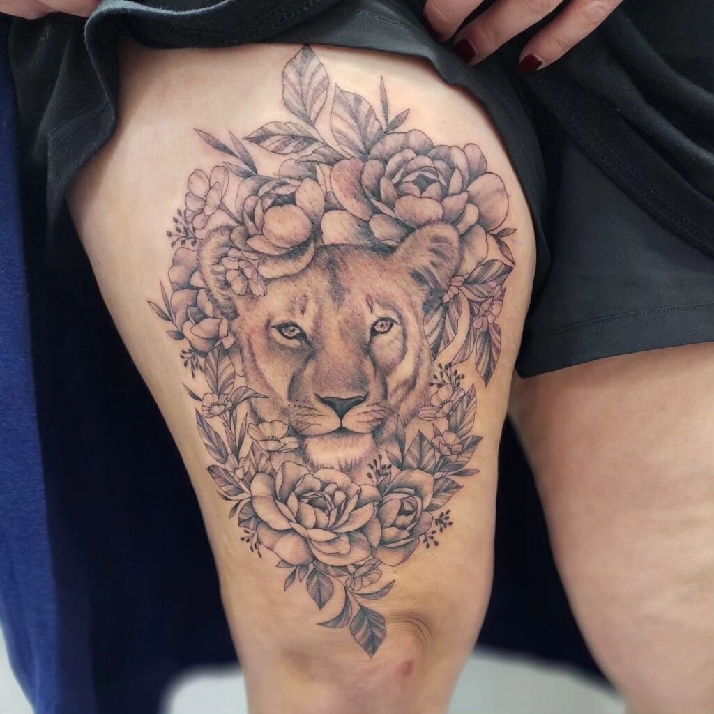 Female lion head surrounded by flowers on the thigh, creating a large canvas of feminine power and beauty motherly grace