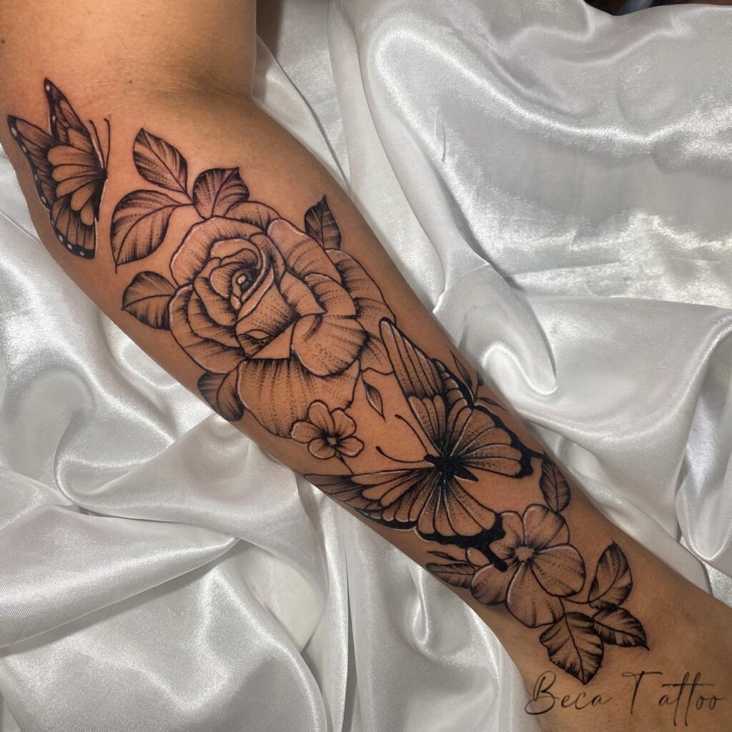Feminine elegance half sleeve tattoo with flowers, butterflies, and roses on the lower arm