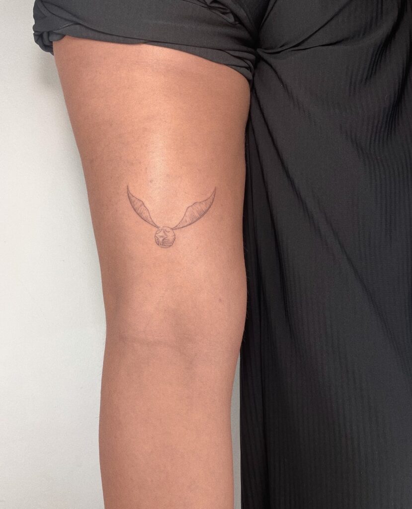 Fine line magic small golden snitch tattoo above the elbow