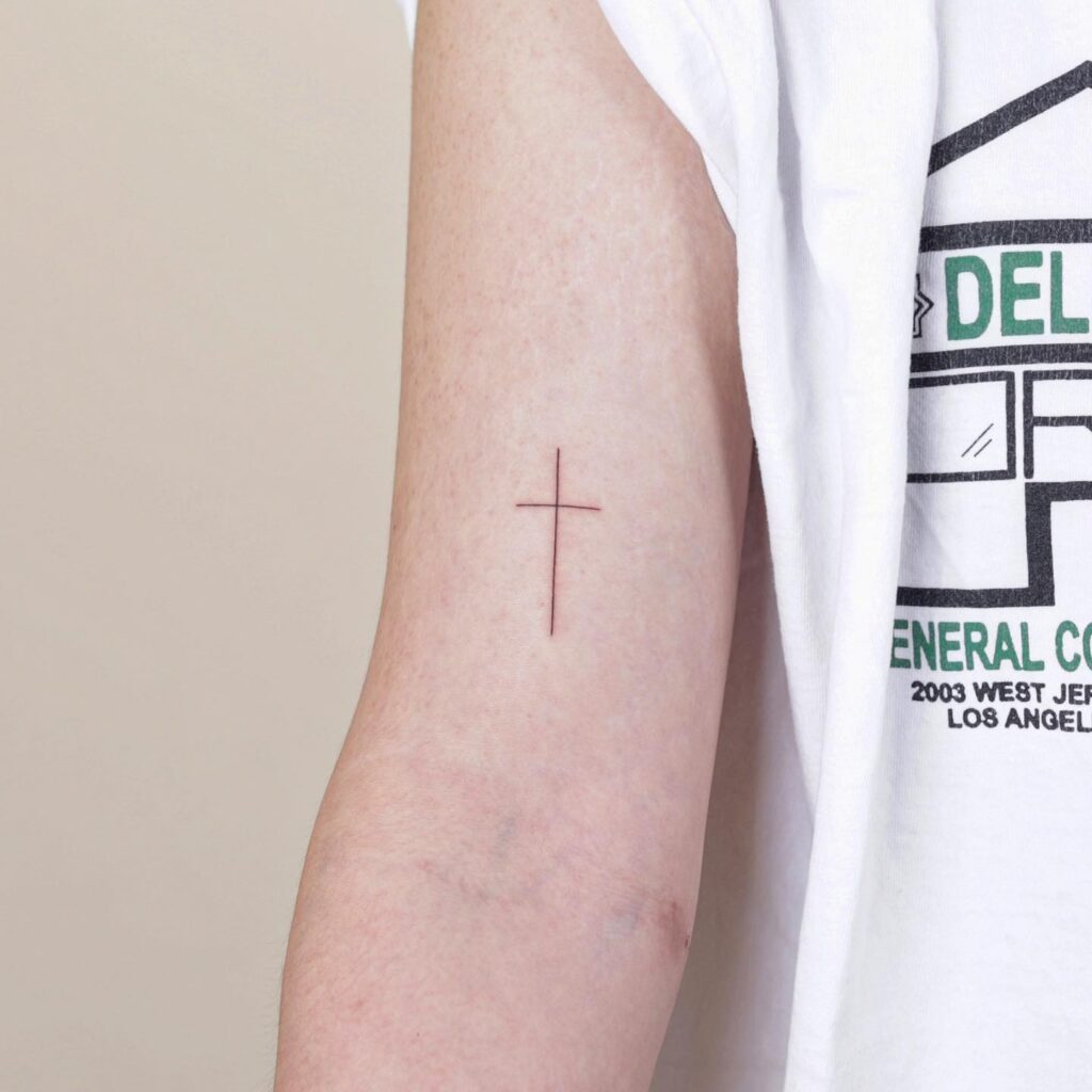 Fineline simple cross tattoo upper elbow girl