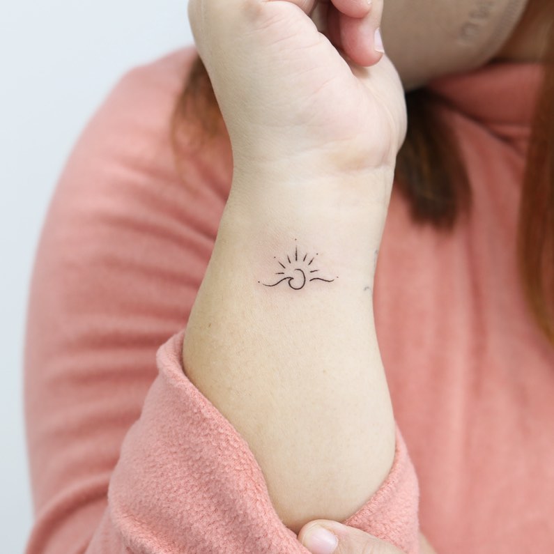 Fineline sunrise and wave tattoo on side wrist ocean-inspired ink