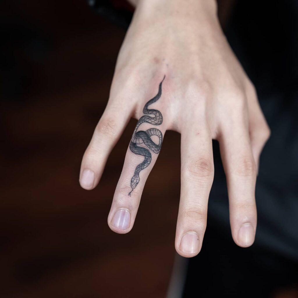 Finger snake tattoo in black and grey on the ring finger serpent's embrace