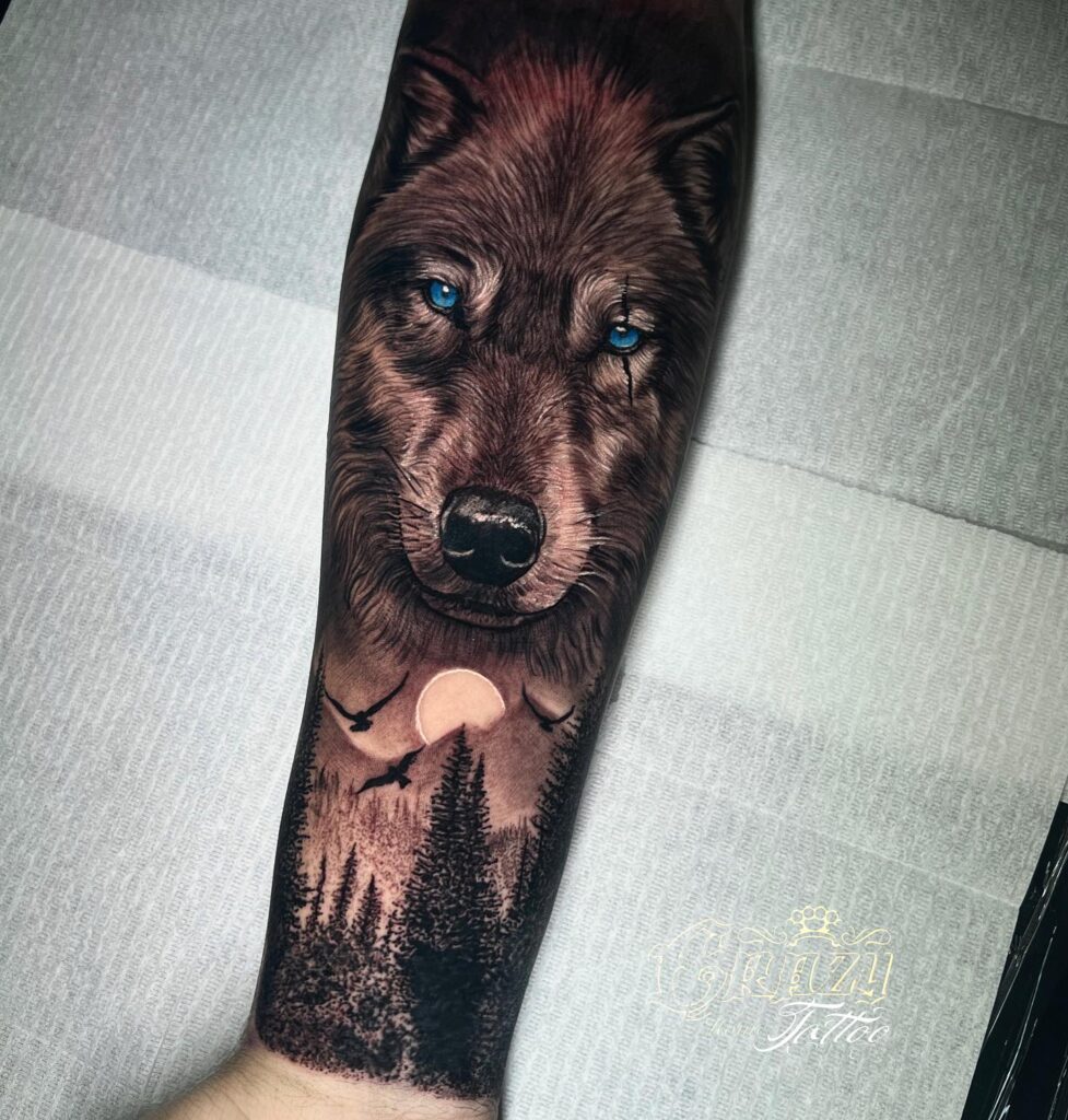 Forearm ink realistic wolf with blue eyes amidst mountains and moon