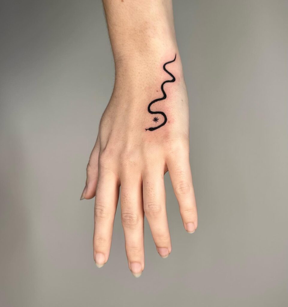 Free-handed snake tattoo on the hand, blackwork ink, featuring a top view, forked tongue, and a small star: serpentine charm