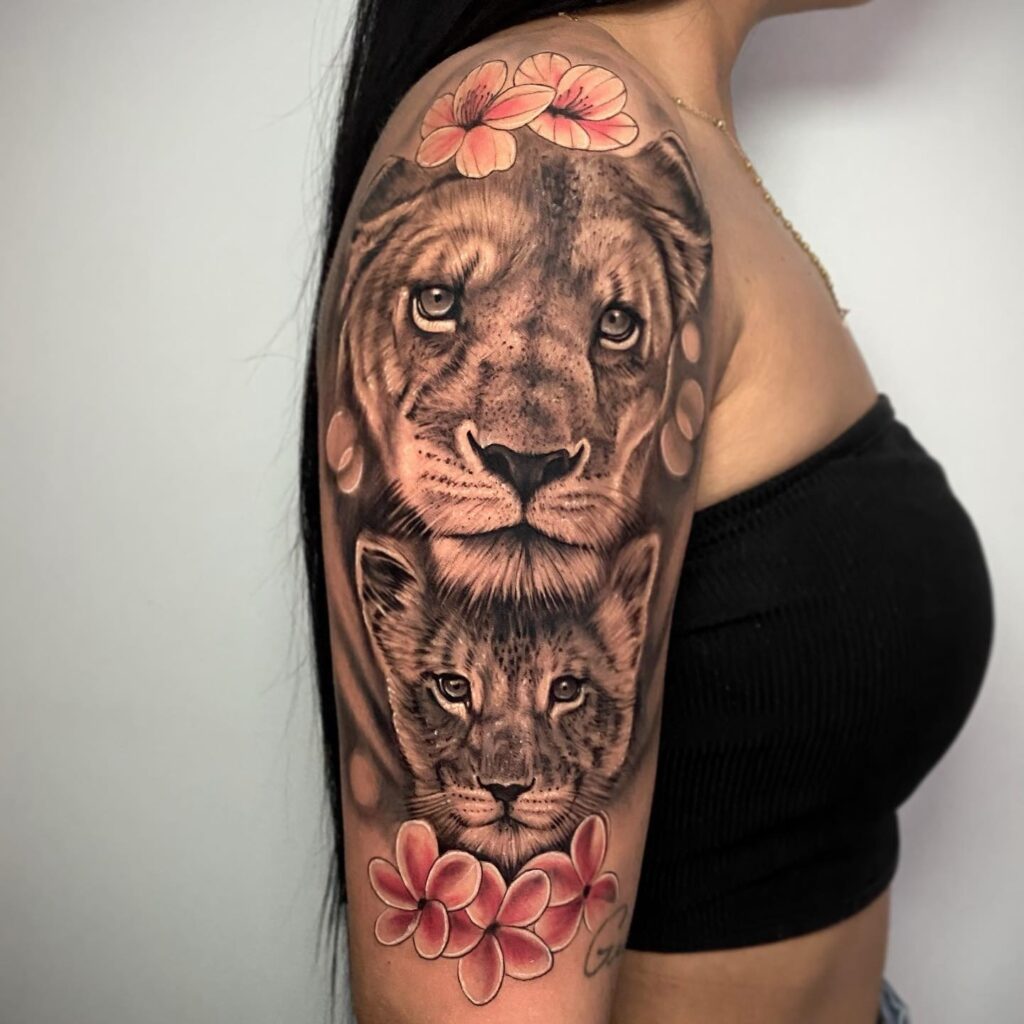 Full covered lion with cub tattoo on the upper arm with floral accents above and below: upper arm royalty