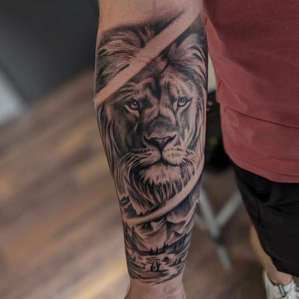 Fully covered lion head tattoo with mountain and river scene on the inner wrist: wild forearm scene