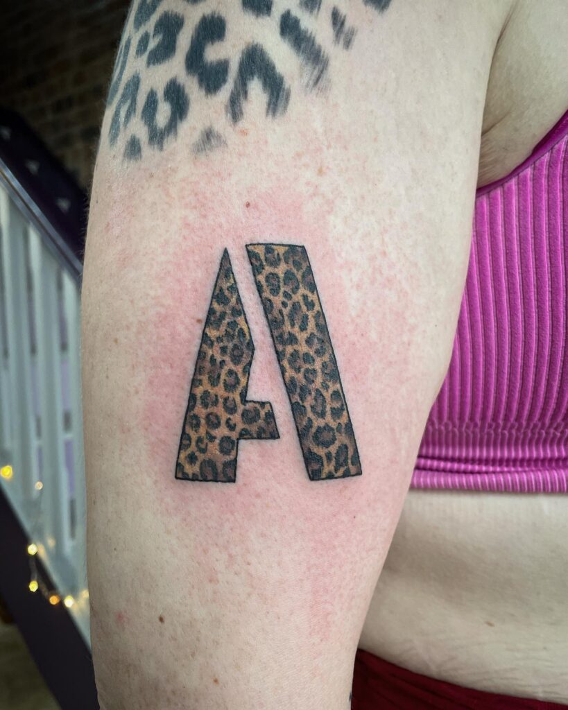 Fusion of Femininity and Strength: Leopard Print Alphabet Symbol Tattoo on Arm