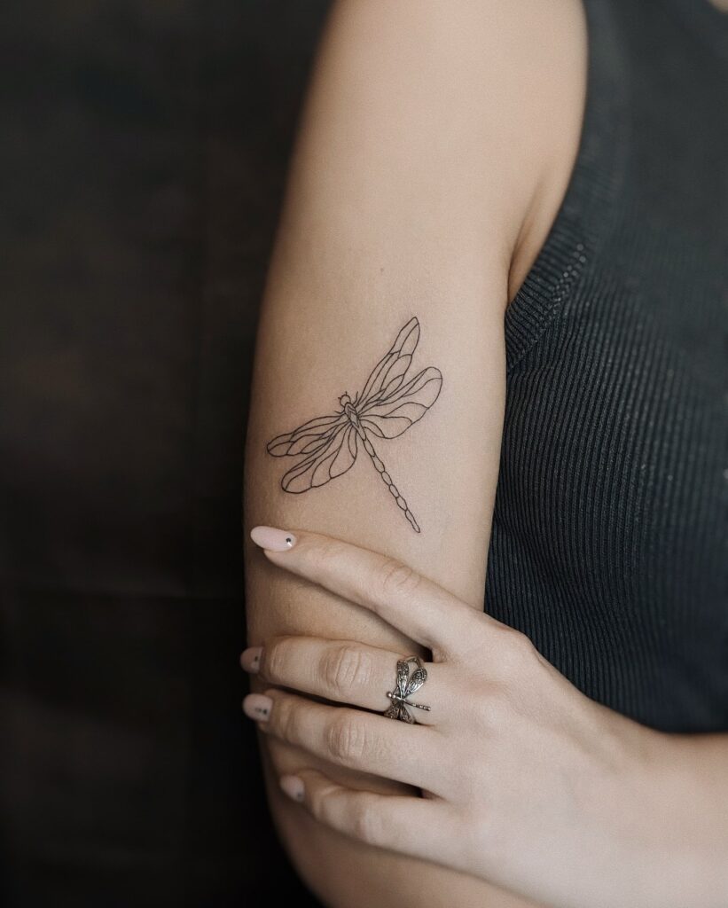 Graceful Upper Arm Dragonfly Tattoo with a Minimalist Fine-Line Design