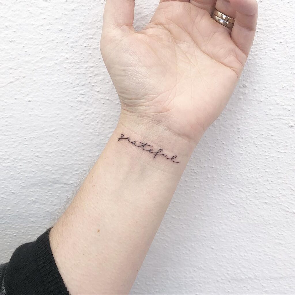 Grateful word script lettering tattoo on the inner wrist, featuring thin script font weight for a delicate touch: graceful gratefulness